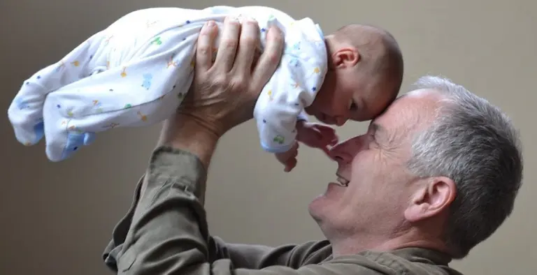 A grey-haired dad lifting his baby above his face, nose to nose