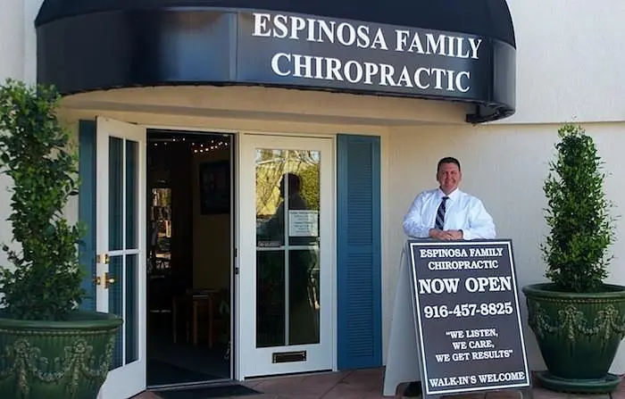 Dr. Espinosa at the front door under the Espinosa Family Chiropractic awning, beside a sidewalk sign